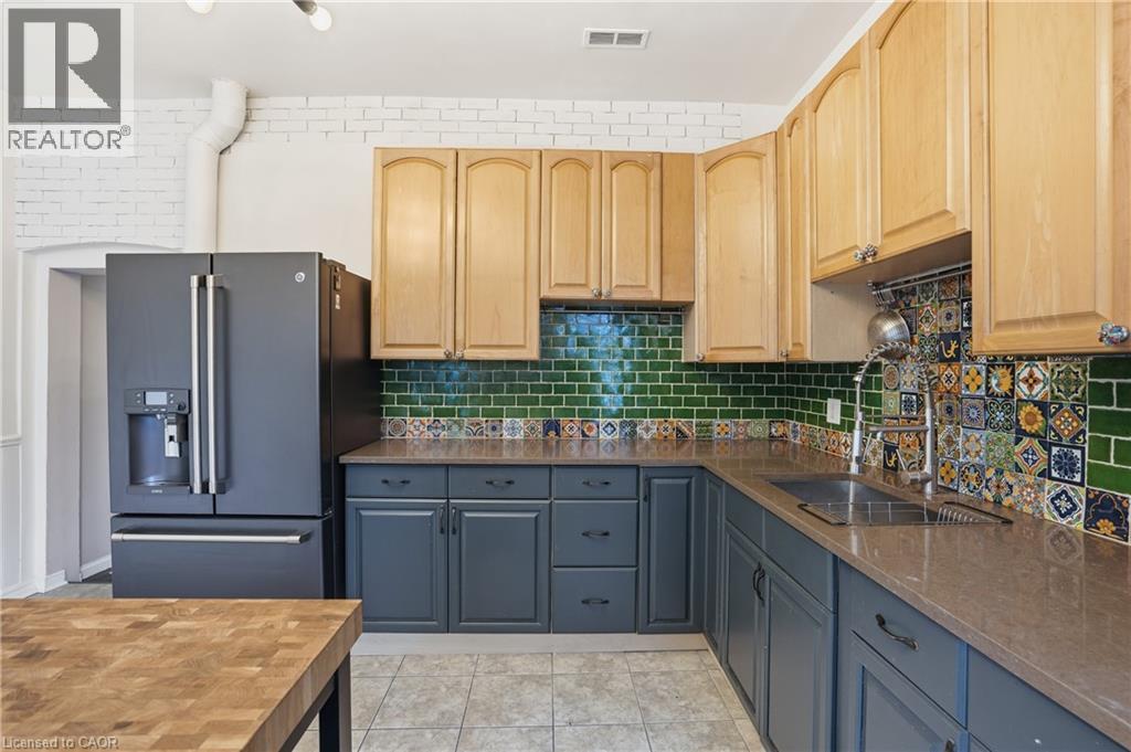 Kitchen with high end refrigerator, decorative backsplash, dark stone counters, light tile patterned floors, and light brown cabinets - 313 Mary Street, Hamilton, ON - Indoor Photo Showing Kitchen With Double Sink