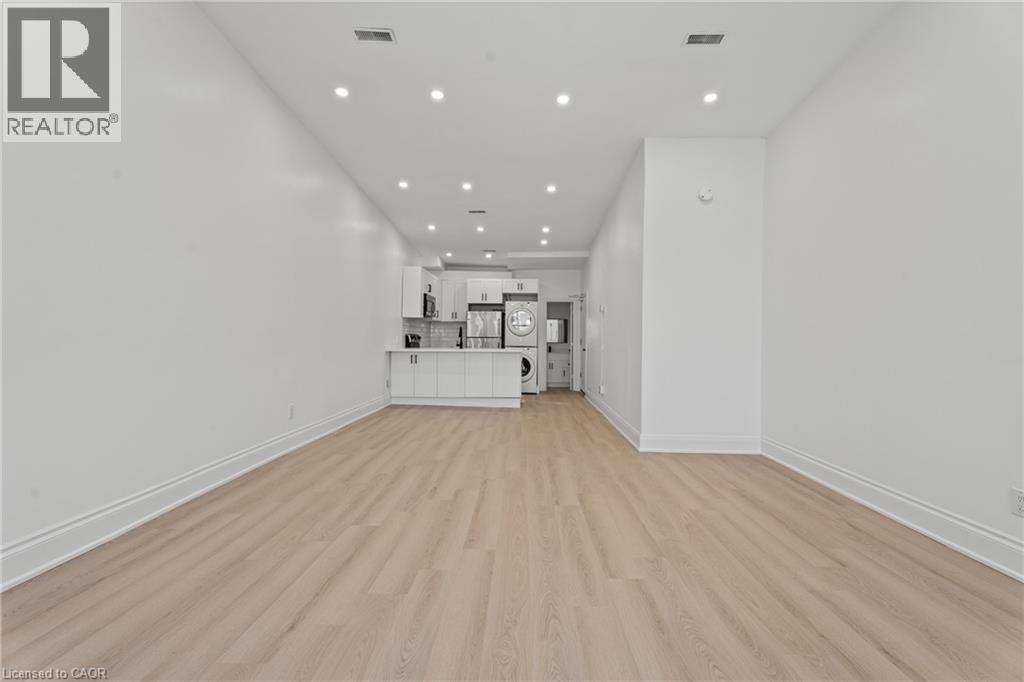 Unfurnished living room with light wood-style floors, recessed lighting, and stacked washing machine and dryer - 93 John Street S, Hamilton, ON