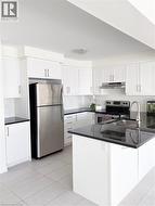 Kitchen with white cabinets, appliances with stainless steel finishes, and dark stone countertops -