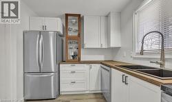 Kitchen featuring stainless steel appliances, white cabinets, butcher block countertops, light wood-style flooring, and glass insert cabinets -