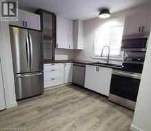 Kitchen featuring stainless steel appliances, white cabinetry, glass insert cabinets, dark countertops, and light wood-type flooring -
