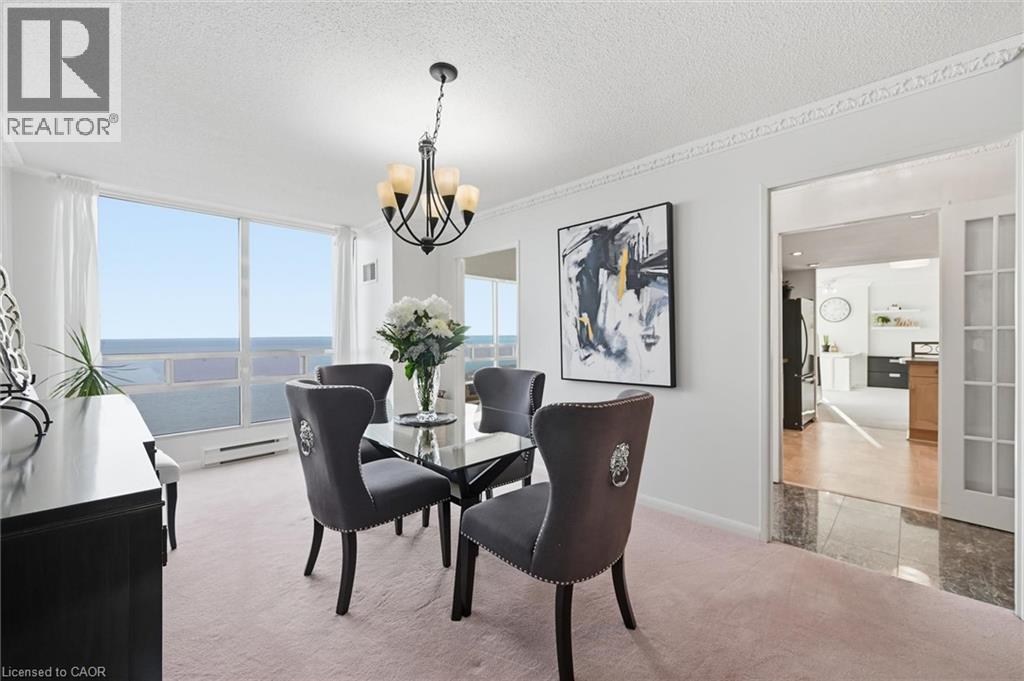 Dining area featuring light carpet, a textured ceiling, a chandelier, baseboard heating, and a water view - 2170 Marine Drive Unit# 1808, Oakville, ON - Indoor Photo Showing Dining Room