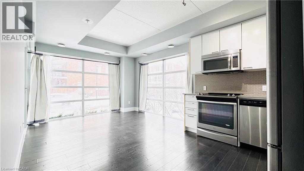 Kitchen with stainless steel appliances, white cabinets, light countertops, and decorative backsplash - 155 St. Leger Unit# 107, Kitchener, ON - Indoor Photo Showing Kitchen