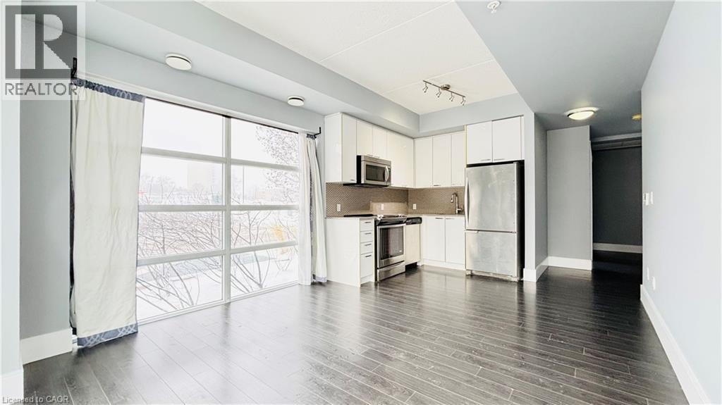Kitchen with stainless steel appliances, white cabinets, dark wood-type flooring, track lighting, and backsplash - 155 St. Leger Unit# 107, Kitchener, ON - Indoor Photo Showing Kitchen