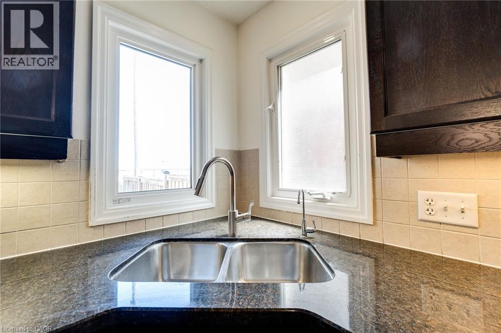 Kitchen featuring dark stone countertops, backsplash, and dark brown cabinetry - 928 Dunblane Court, Kitchener, ON - Indoor Photo Showing Kitchen With Double Sink
