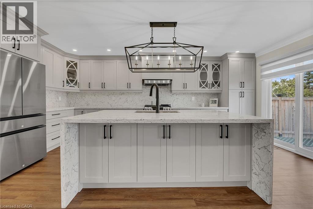 Kitchen with glass insert cabinets, light stone counters, tasteful backsplash, freestanding refrigerator, and a spacious island - 125 Valera Drive, Hamilton, ON - Indoor Photo Showing Kitchen With Upgraded Kitchen