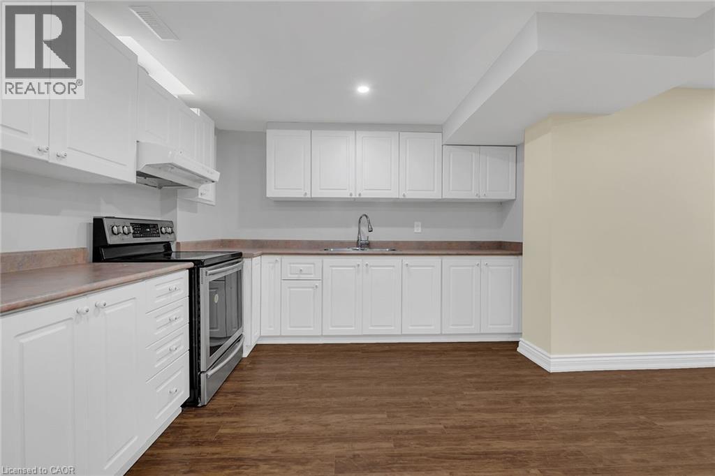 Kitchen with stainless steel electric stove, under cabinet range hood, dark wood-style floors, white cabinetry, and recessed lighting - 125 Valera Drive, Hamilton, ON - Indoor Photo Showing Kitchen