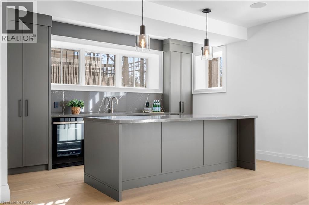 Indoor wet bar with gray cabinetry, light wood-style flooring, tasteful backsplash, wine cooler, and pendant lighting - 1322 Minaki Road, Mississauga, ON - Indoor Photo Showing Kitchen