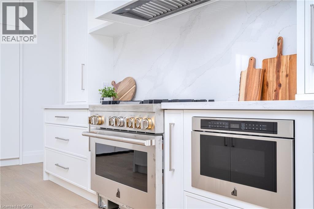 Kitchen with white cabinets, appliances with stainless steel finishes, light wood-style floors, light stone countertops, and custom exhaust hood - 1322 Minaki Road, Mississauga, ON - Indoor