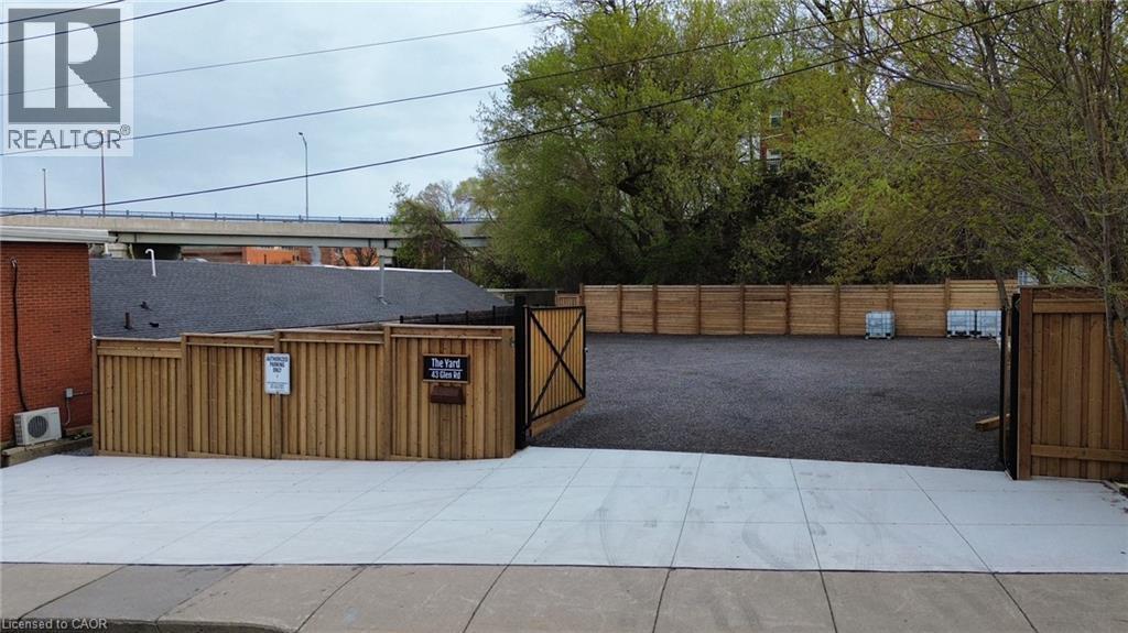 Paved concrete entrance leading to a secure, fenced outdoor area with a dark gravel surface - 43 Glen Road, Hamilton, ON