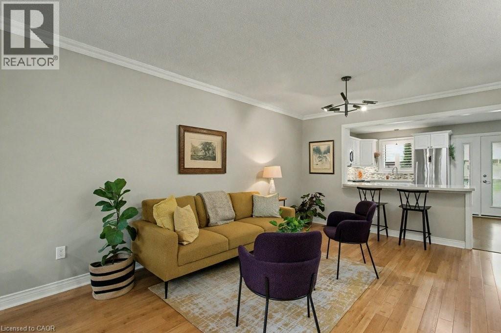 Living room with a textured ceiling, crown molding, light wood-style floors, and a chandelier - 165 Main Street E Unit# 9, Grimsby, ON - Indoor Photo Showing Living Room