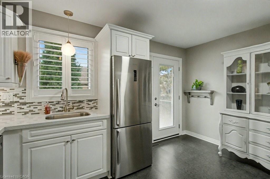 Kitchen with white cabinets, freestanding refrigerator, pendant lighting, tasteful backsplash, and light stone counters - 165 Main Street E Unit# 9, Grimsby, ON - Indoor Photo Showing Kitchen