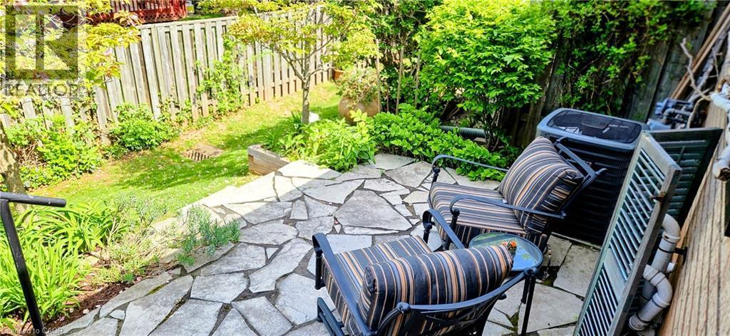 Flagstone patio with a manicured lawn, established perimeter fencing, and mature shrubbery - 165 Main Street E Unit# 9, Grimsby, ON - Outdoor With Deck Patio Veranda