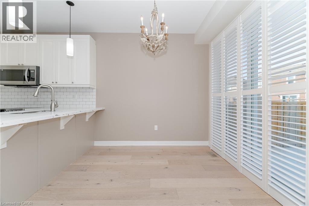 Kitchen featuring decorative backsplash, a breakfast bar area, light wood finished floors, a chandelier, and stainless steel microwave - 28 Pickett Place, Cambridge, ON - Indoor Photo Showing Kitchen