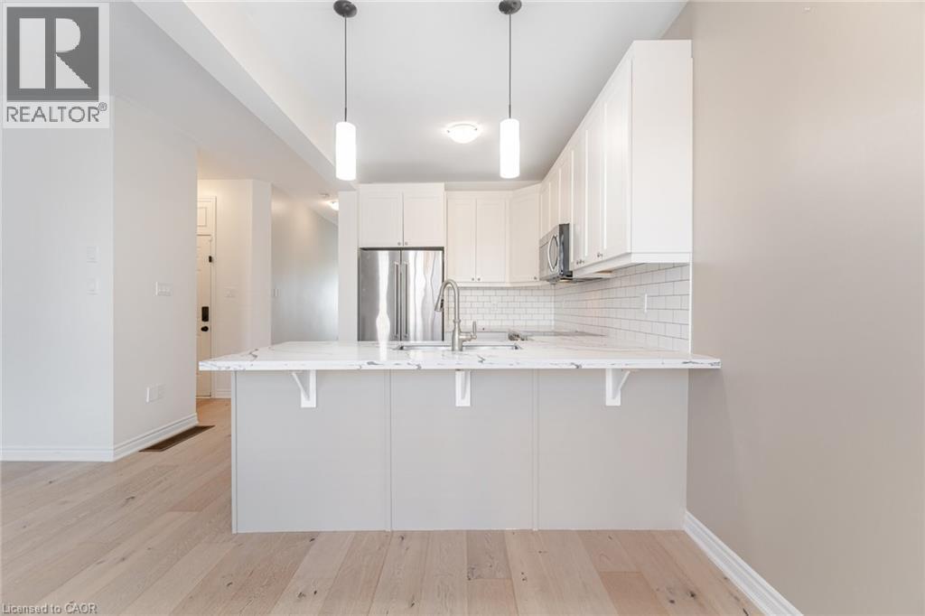 Kitchen with decorative backsplash, light wood finished floors, white cabinets, a breakfast bar area, and pendant lighting - 28 Pickett Place, Cambridge, ON - Indoor Photo Showing Kitchen With Upgraded Kitchen