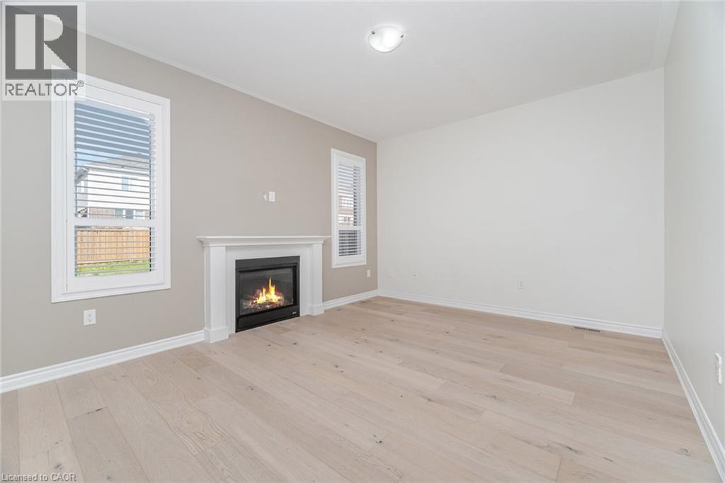 Unfurnished living room with healthy amount of natural light, light wood-style floors, and a glass covered fireplace - 28 Pickett Place, Cambridge, ON - Indoor Photo Showing Other Room With Fireplace