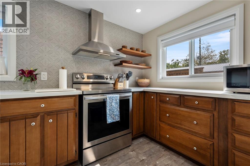 Kitchen with brown cabinetry, stainless steel appliances, wall chimney exhaust hood, light countertops, and dark wood-type flooring - 197 Cedar Drive, Turkey Point, ON - Indoor Photo Showing Kitchen
