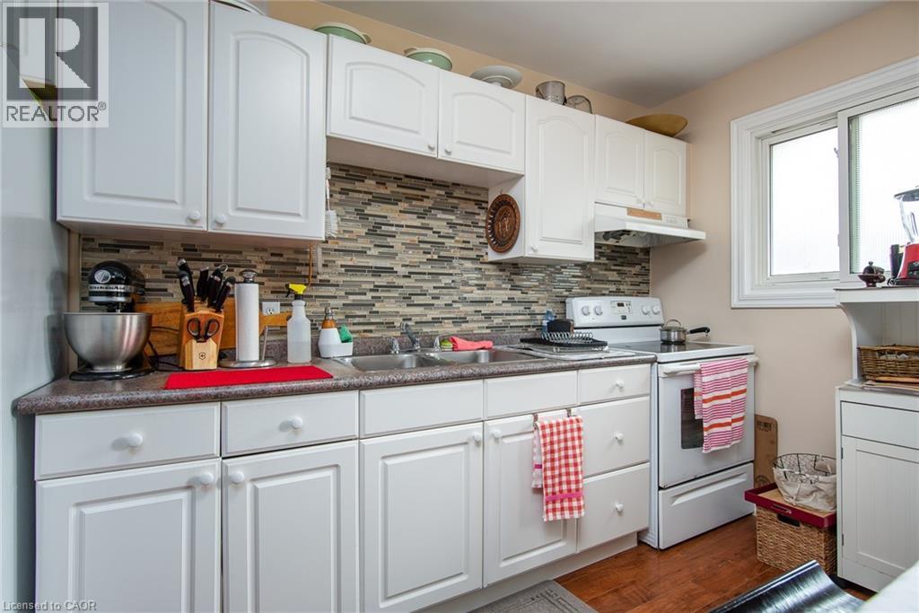 Kitchen featuring white electric range oven, under cabinet range hood, tasteful backsplash, and white cabinets - 129 River Road E, Kitchener, ON - Indoor Photo Showing Kitchen With Double Sink