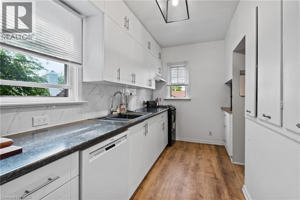 Kitchen with dishwasher, black range with gas cooktop, dark countertops, light wood-style flooring, and tasteful backsplash - 5368 Menzie Street, Niagara Falls, ON - Indoor Photo Showing Kitchen With Double Sink