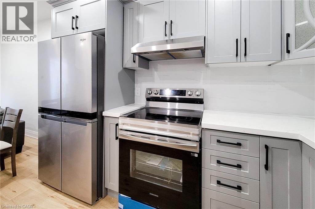 Kitchen with stainless steel appliances, gray cabinets, under cabinet range hood, and light wood-type flooring - 51 West Avenue N, Hamilton, ON - Indoor Photo Showing Kitchen