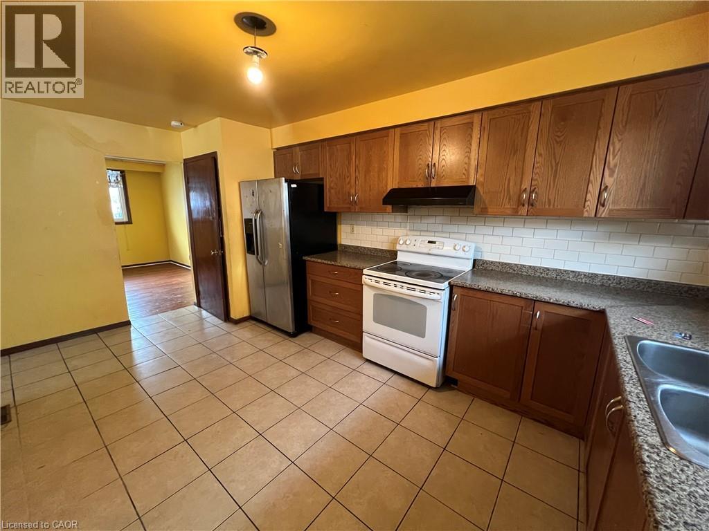 Eat-in Kitchen featuring electric stove, dark countertops, light tile patterned floors, tasteful backsplash, and wood finish cabinetry - 185 Lavina Crescent, Hamilton, ON - Indoor Photo Showing Kitchen With Double Sink