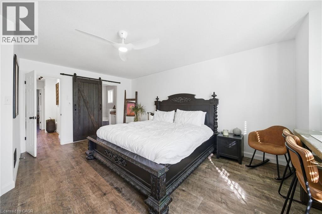 Bedroom with a barn door, dark wood finished floors, ceiling fan, and ensuite bathroom - 136 Braemar Avenue, Caledonia, ON - Indoor Photo Showing Bedroom