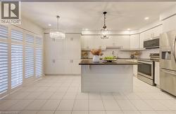 Kitchen featuring appliances with stainless steel finishes, a center island, light tile patterned flooring, decorative backsplash, and decorative light fixtures -
