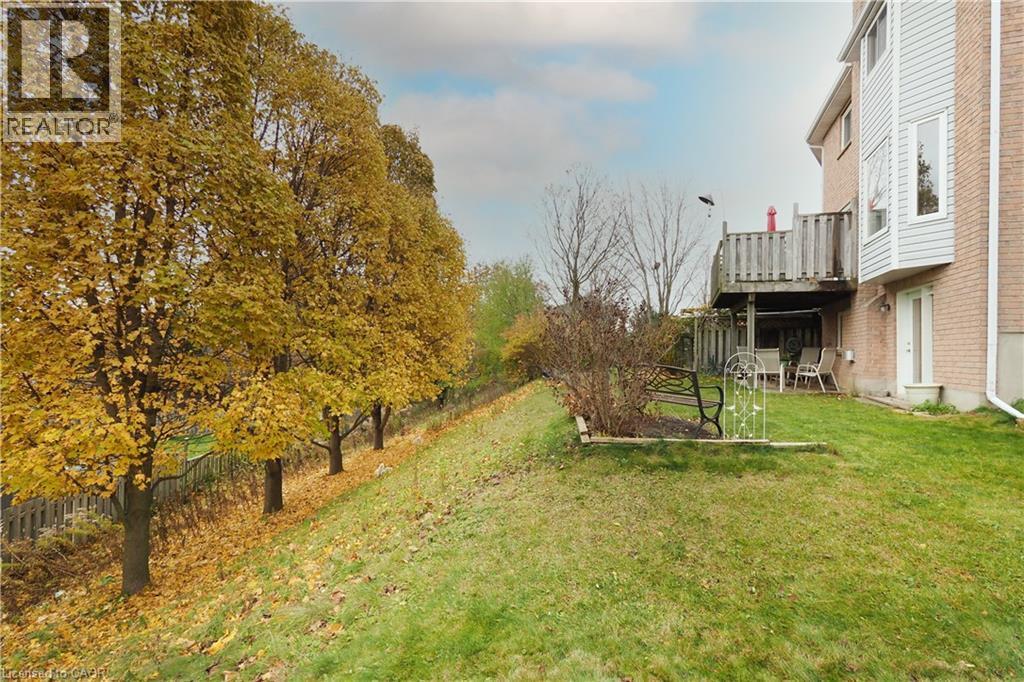 View of spacious lawn bordered by mature trees and featuring a lower level patio area and main floor wooden deck - 511 Oakvale Drive Unit# 1, Waterloo, ON - Outdoor
