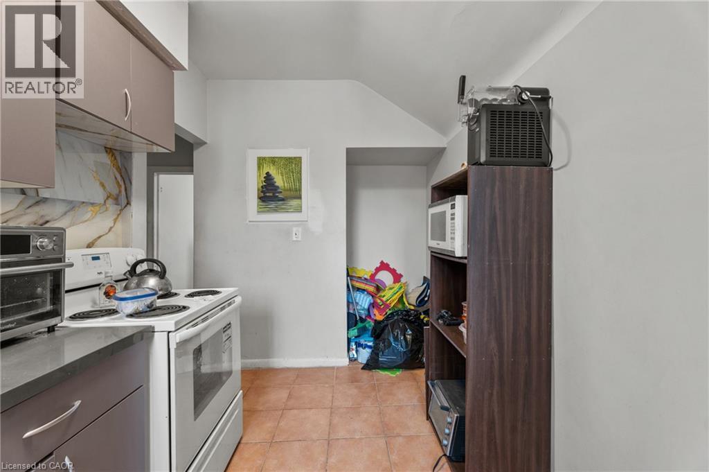 Kitchen featuring white appliances, light tile patterned floors, vaulted ceiling, dark countertops, and gray cabinets - 246 Mary Street, Hamilton, ON