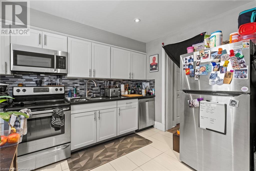 Kitchen with backsplash, a sink, light tile patterned floors, stainless steel appliances, and white cabinets - 181 West Avenue N, Hamilton, ON - Indoor Photo Showing Kitchen With Double Sink
