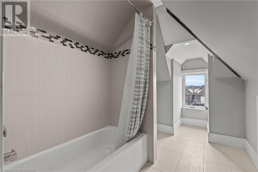 Full bathroom with tile patterned floors, vaulted ceiling, shower / tub combo with curtain, and baseboards - 181 West Avenue N, Hamilton, ON - Indoor Photo Showing Bathroom