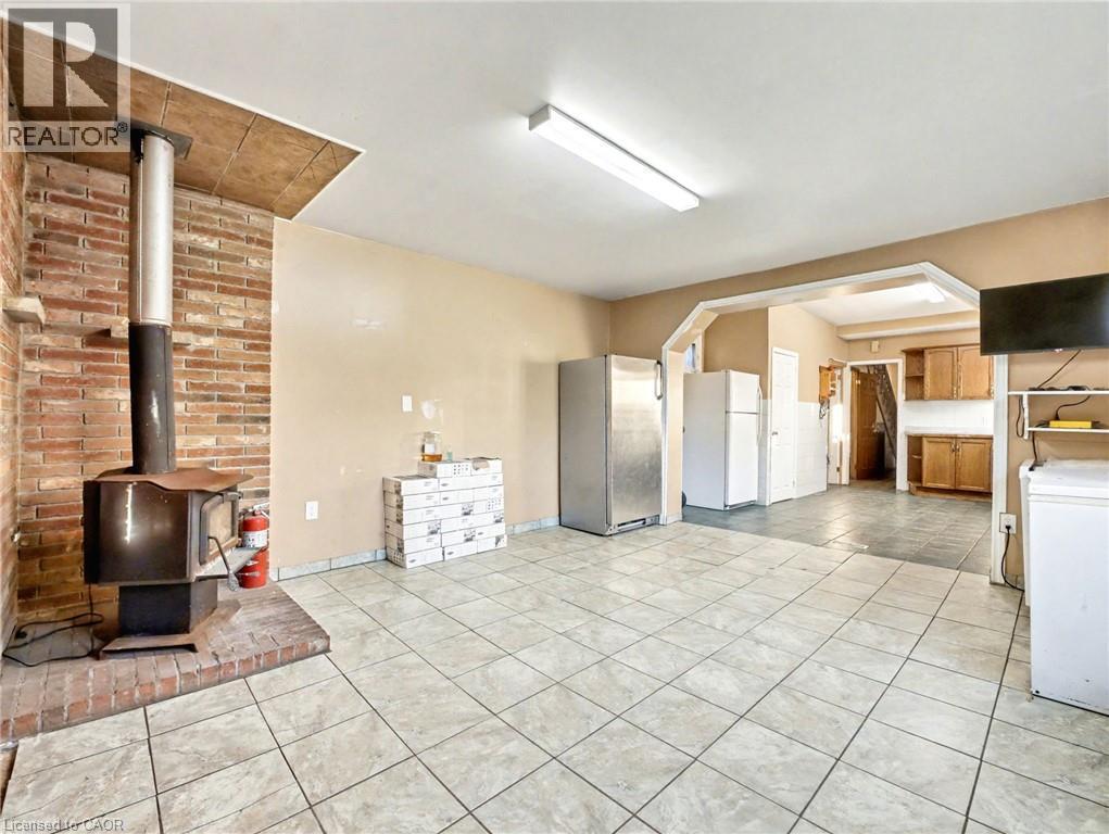 Kitchen with light tile patterned floors, a wood stove, freestanding refrigerator, and light countertops - 23 Oak Avenue, Hamilton, ON - Indoor Photo Showing Other Room