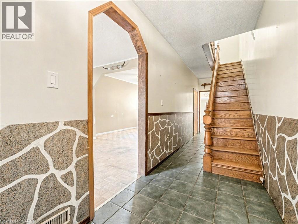 Stairs featuring tile patterned floors, a textured ceiling, wainscoting, and arched walkways - 23 Oak Avenue, Hamilton, ON - Indoor Photo Showing Other Room