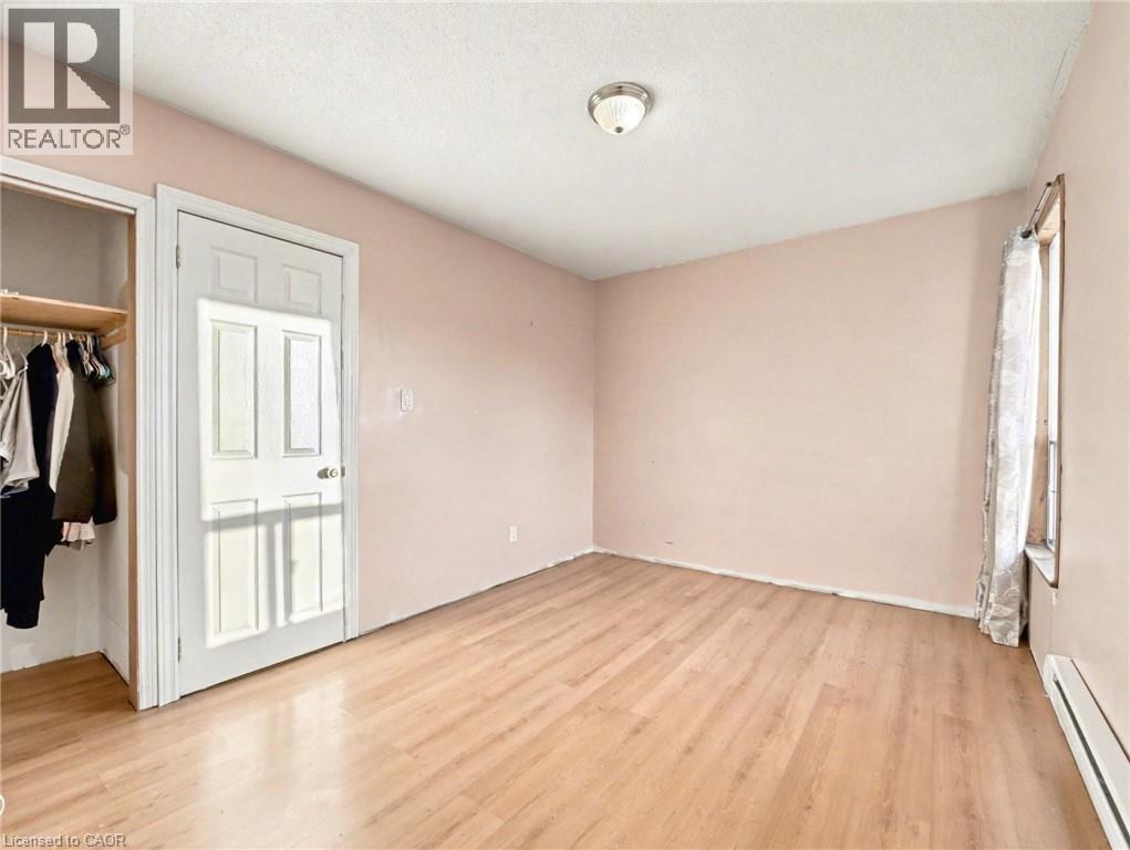 Unfurnished bedroom featuring a baseboard radiator, light wood-style floors, and a textured ceiling - 23 Oak Avenue, Hamilton, ON - Indoor Photo Showing Other Room