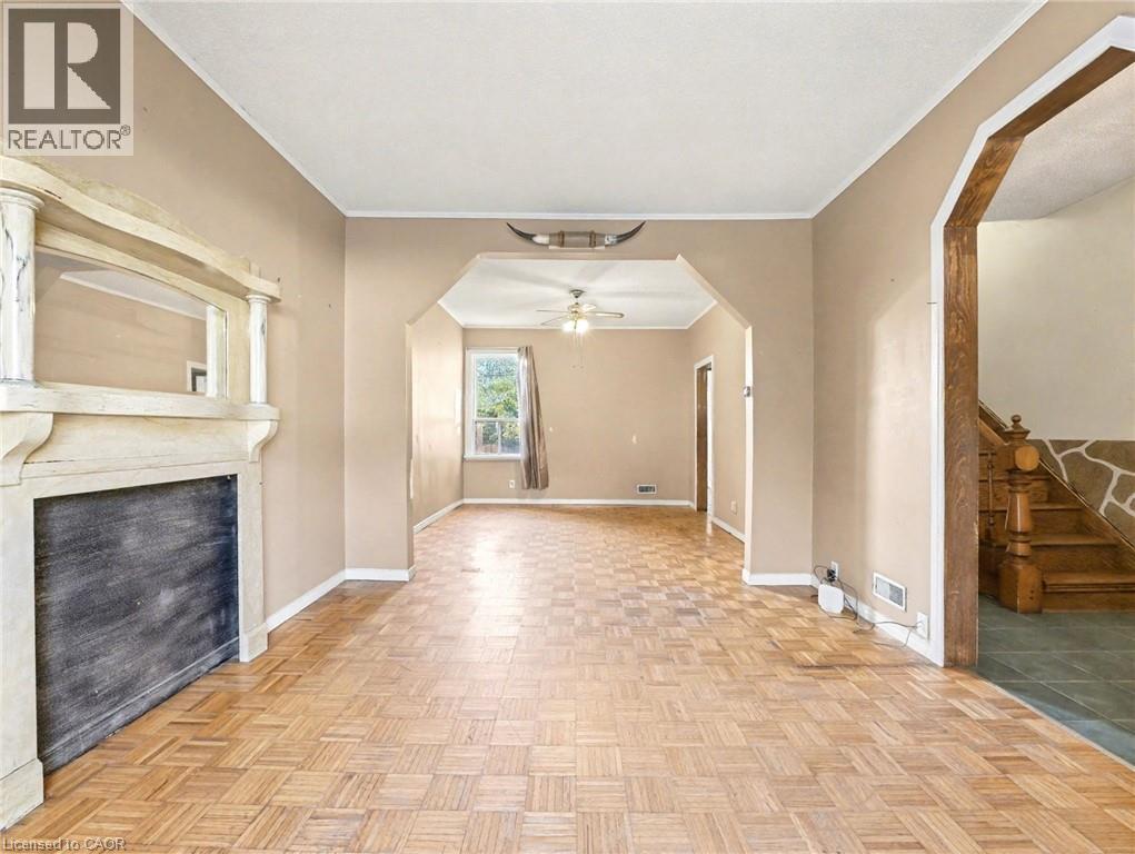 Unfurnished living room with crown molding, arched walkways, a ceiling fan, a fireplace, and stairs - 23 Oak Avenue, Hamilton, ON - Indoor Photo Showing Other Room With Fireplace