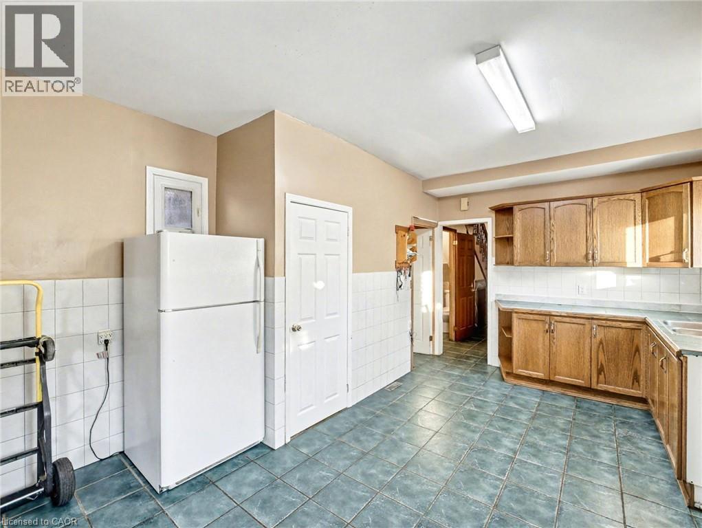 Kitchen featuring freestanding refrigerator, open shelves, tile counters, dark tile patterned floors, and tile walls - 23 Oak Avenue, Hamilton, ON - Indoor Photo Showing Kitchen