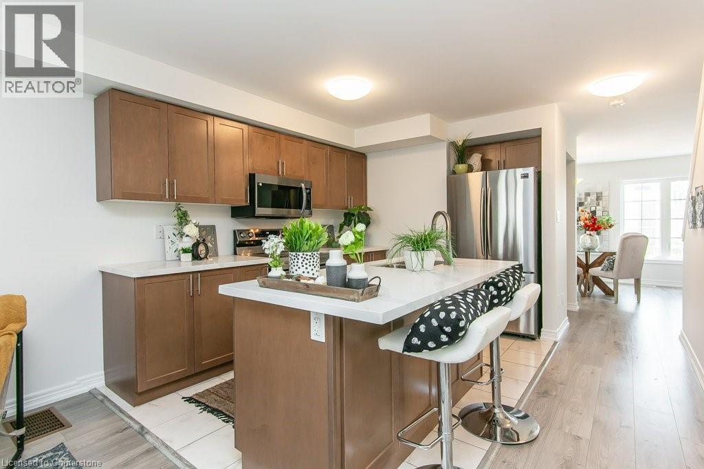 Kitchen with quartz countertop and stainless steel appliances, brown cabinetry, light countertops, light wood-style floors, and a breakfast bar - 386 Linden Drive, Cambridge, ON - Indoor Photo Showing Kitchen