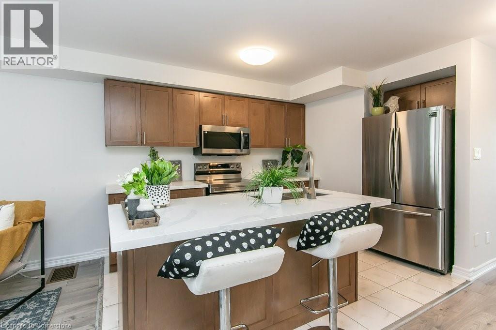 Kitchen featuring appliances with stainless steel finishes, a breakfast bar, a kitchen island, light wood finished floors, and brown cabinets - 386 Linden Drive, Cambridge, ON - Indoor Photo Showing Kitchen