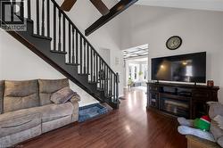 Living room featuring stairway, wood finished floors, ceiling fan, a high ceiling, and beam ceiling -