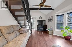 Living area featuring stairs, vaulted ceiling, ceiling fan, dark wood-type flooring, and healthy amount of natural light -