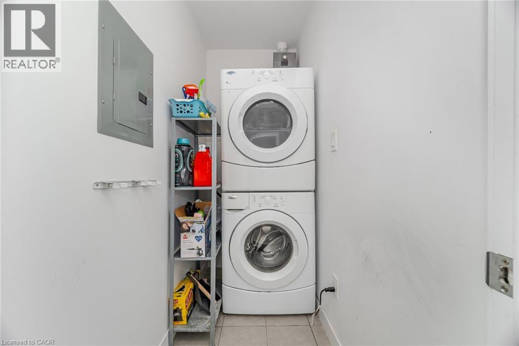 Laundry area with tile patterned flooring, electric panel, and stacked washer and clothes dryer - 5317 Upper Middle Road Unit# 112, Burlington, ON - Indoor Photo Showing Laundry Room