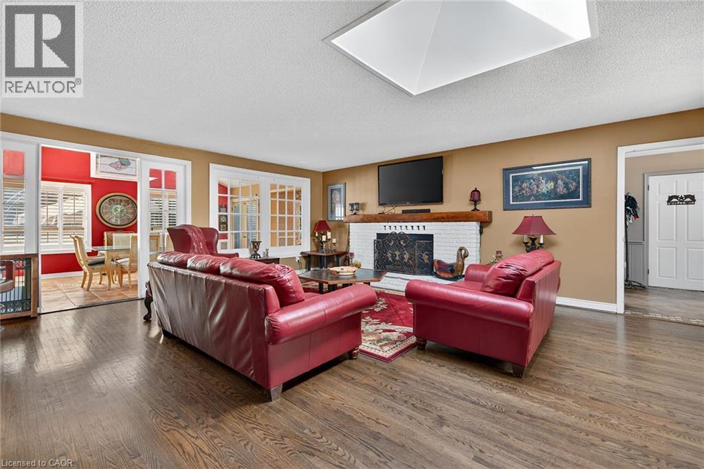 Living area featuring a textured ceiling, wood finished floors, a brick fireplace, healthy amount of natural light, and a skylight - 5590 Blind Line, Burlington, ON - Indoor Photo Showing Living Room With Fireplace