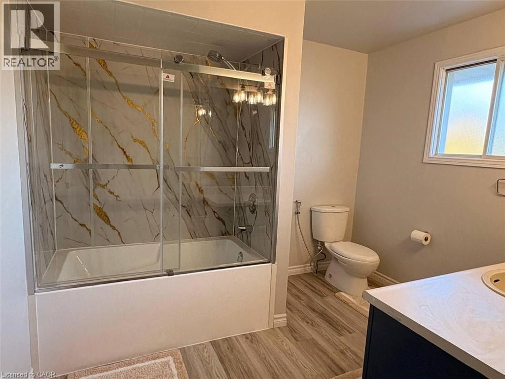 Bathroom with vanity, bath / shower combo with glass door, and wood finished floors - 14 Windstar Place Unit# Upper, Hamilton, ON - Indoor Photo Showing Bathroom