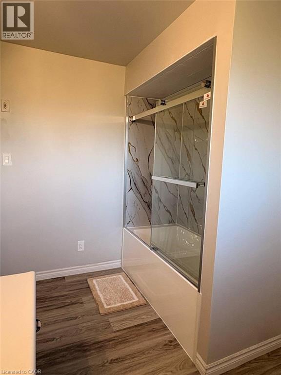 Full bath featuring wood finished floors and bath / shower combo with glass door - 14 Windstar Place Unit# Upper, Hamilton, ON - Indoor