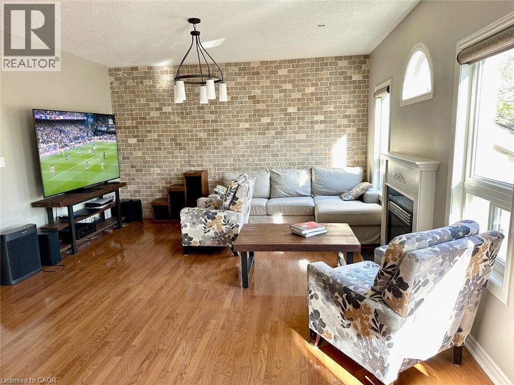 Living room featuring wood finished floors, a textured ceiling, brick wall, and a glass covered fireplace - 2429 Whitehorn Drive, Burlington, ON - Indoor Photo Showing Living Room