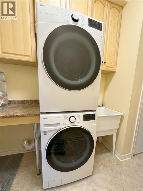 Washroom featuring stacked washer and clothes dryer, cabinet space, and light tile patterned floors - 2429 Whitehorn Drive, Burlington, ON - Indoor Photo Showing Laundry Room