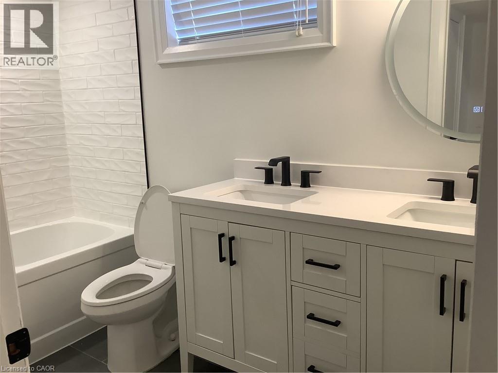 Full bath with double vanity, washtub / shower combination, and dark tile patterned floors - 229 West 18Th Street, Hamilton, ON - Indoor Photo Showing Bathroom