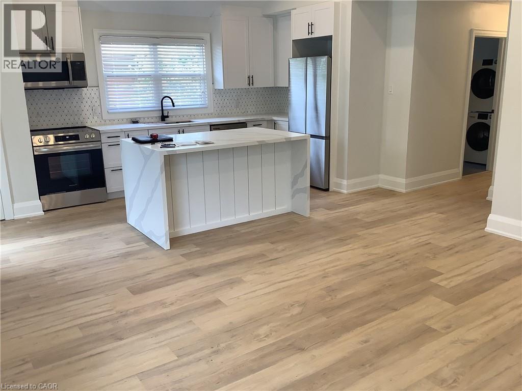 Kitchen with a center island, stainless steel appliances, white cabinets, light stone counters, and light wood finished floors - 229 West 18Th Street, Hamilton, ON - Indoor Photo Showing Kitchen With Stainless Steel Kitchen With Upgraded Kitchen