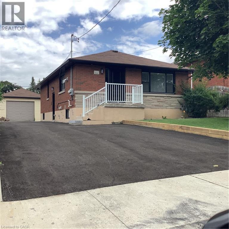 Bungalow-style house featuring an outdoor structure, brick siding, asphalt driveway, and a detached garage - 229 West 18Th Street, Hamilton, ON - Outdoor