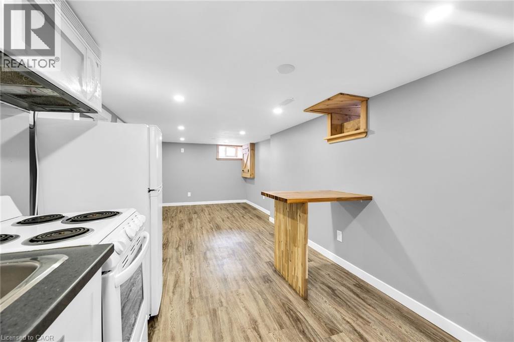 Kitchen featuring white appliances, white cabinets, light wood finished floors, baseboards, and dark countertops - 129 Dundurn Street N, Hamilton, ON - Indoor